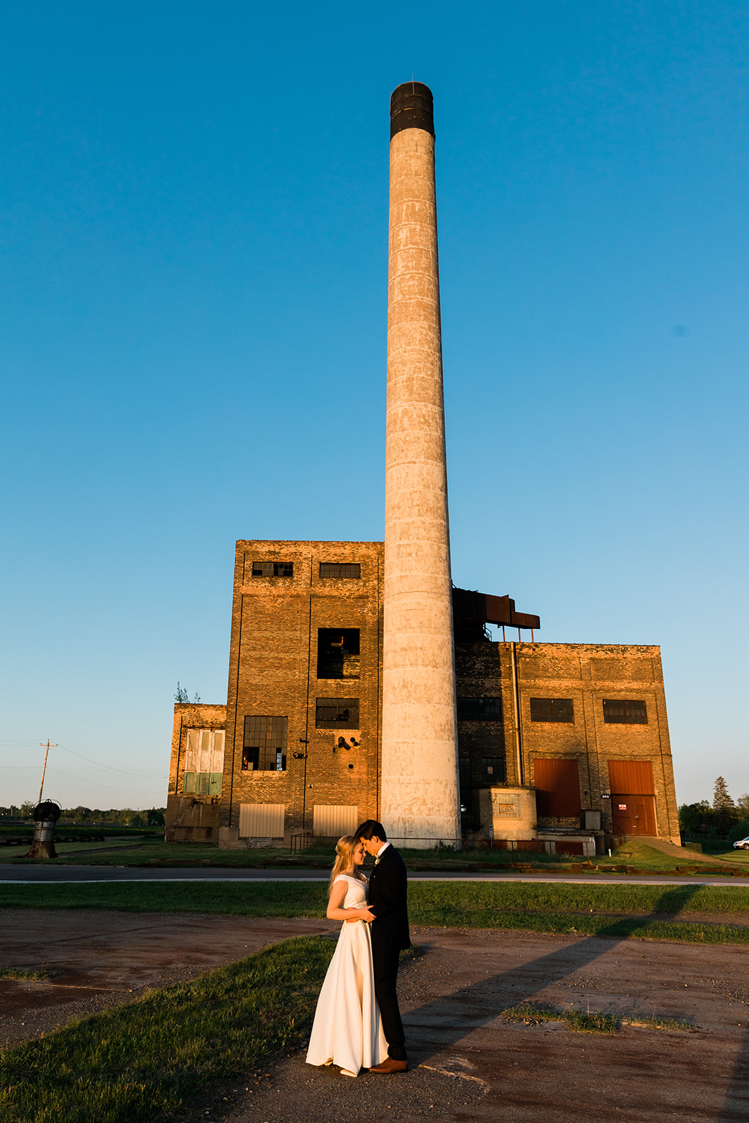 Couple kissing in front of the smokestack and industrial building at golden hour — Tim Larsen Photography, Brainerd Lakes MN