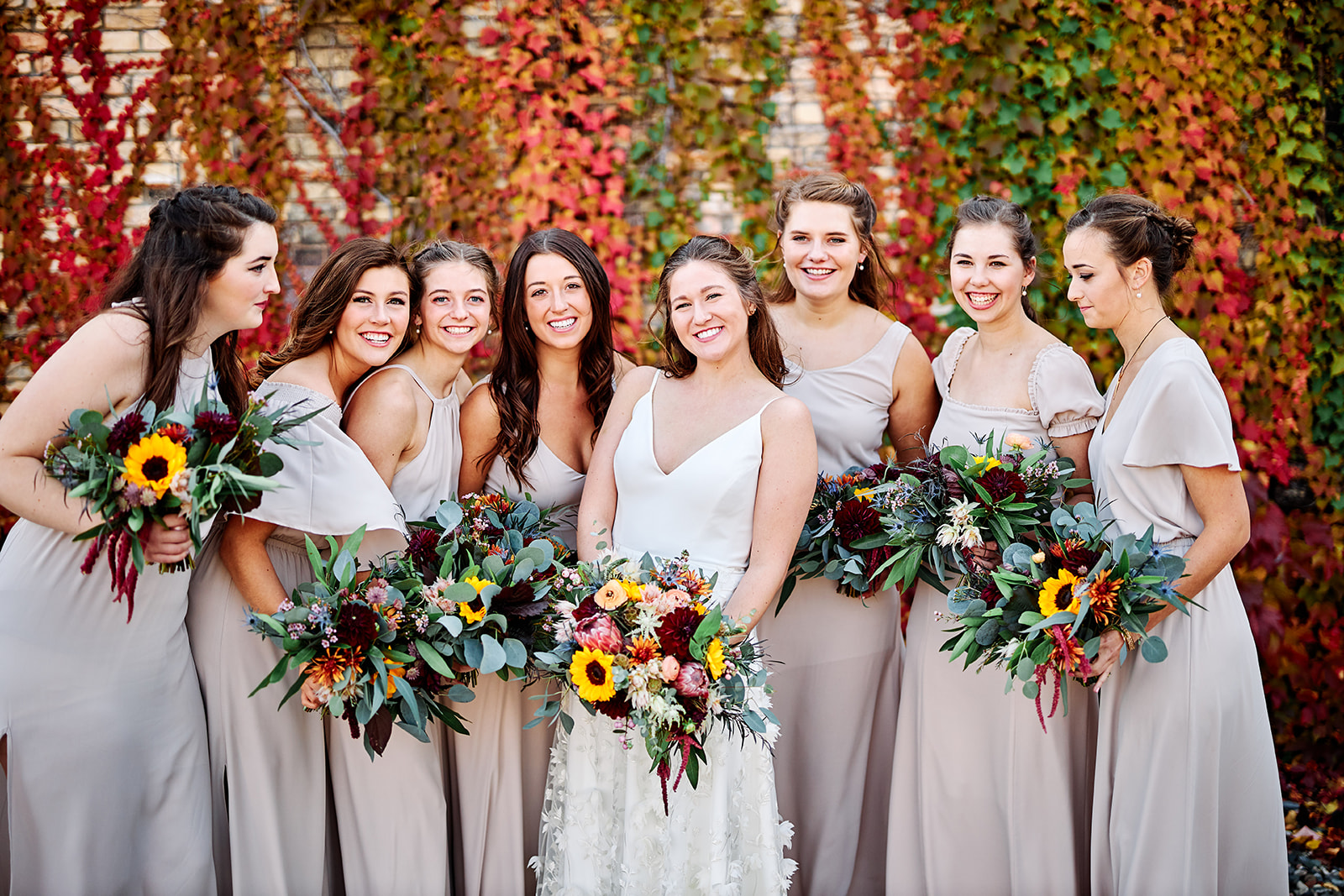 Bride with bridesmaids in neutral dresses against the red ivy wall — sunflower bouquets — Tim Larsen Photography, Brainerd Lakes MN