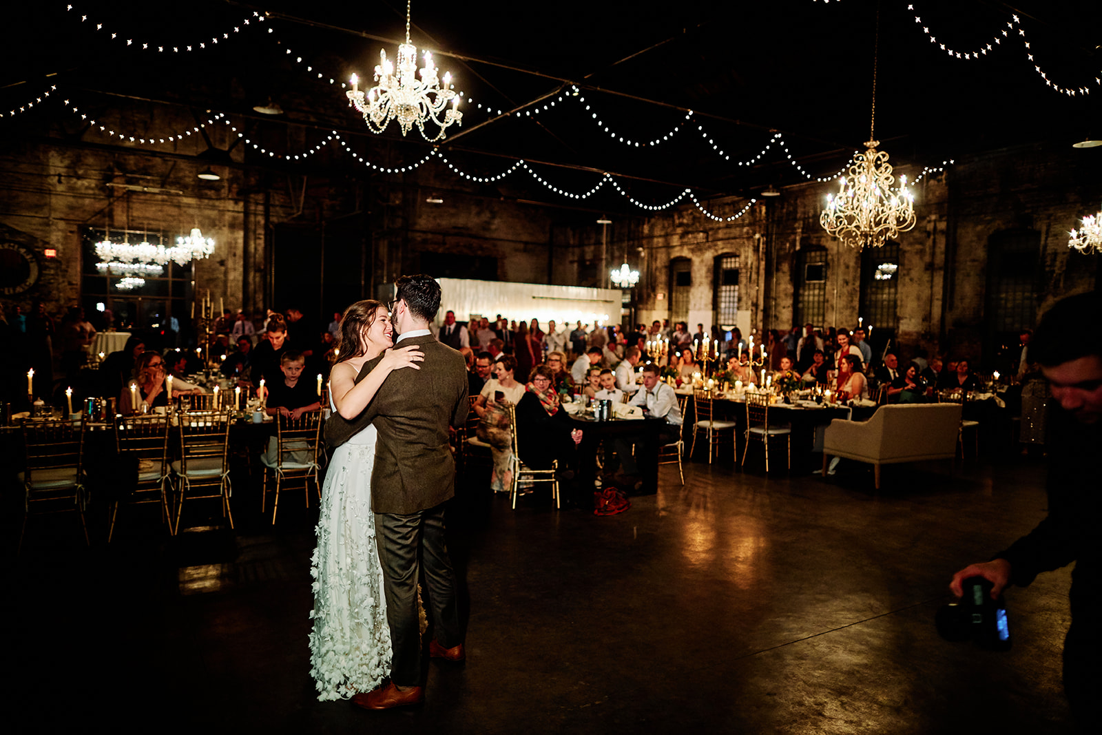 Couple first dance in Blacksmith Main — guests watching under chandeliers and string lights — Tim Larsen Photography, Brainerd Lakes MN