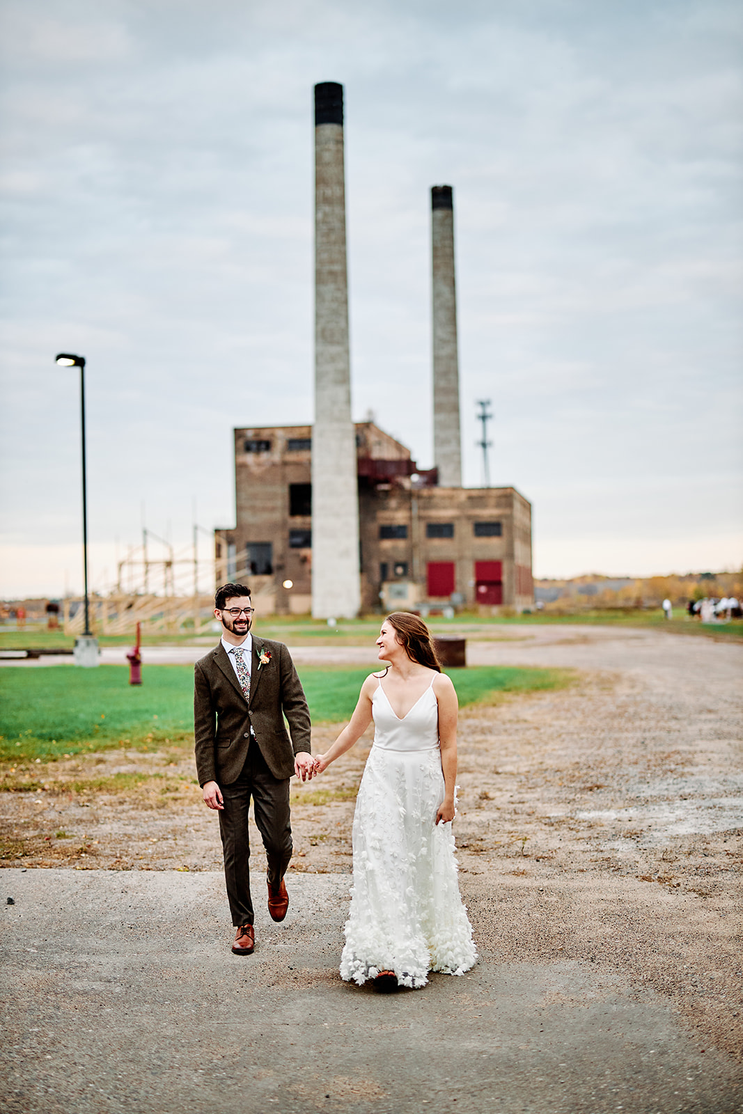 Couple walking hand in hand on the gravel road with smokestacks behind — fall evening — Tim Larsen Photography, Brainerd Lakes MN