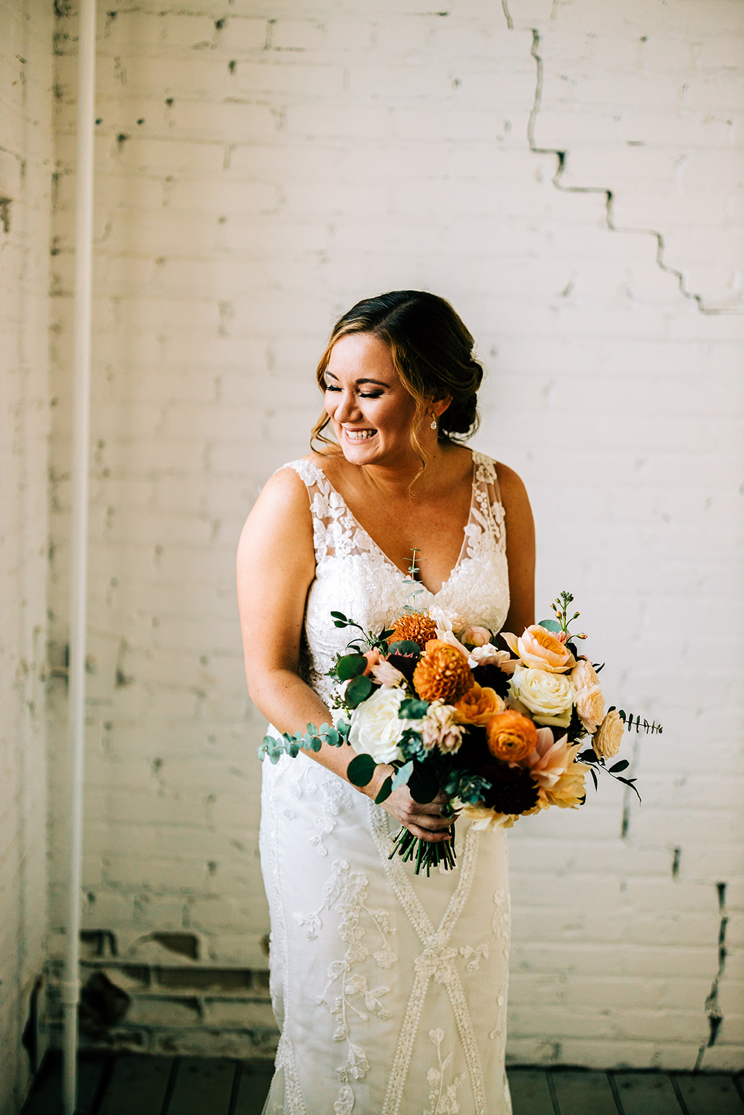 Bridal portrait with orange and cream bouquet against the white brick wall — Tim Larsen Photography, Brainerd Lakes MN