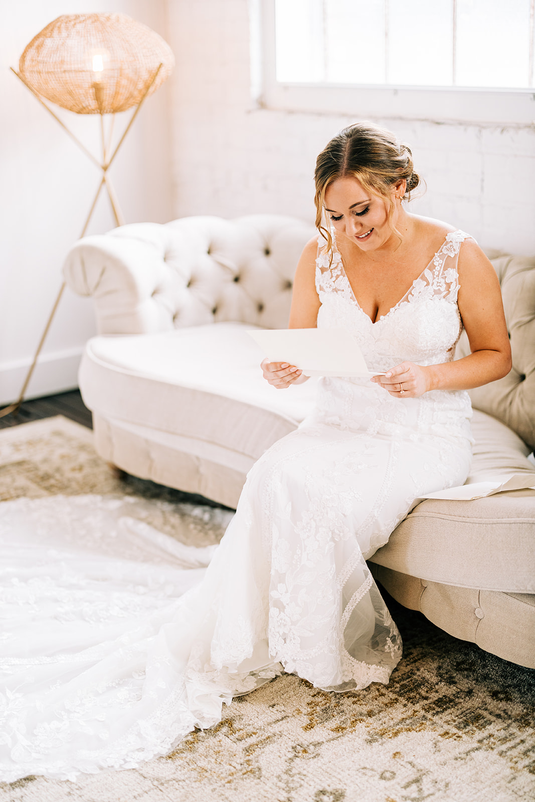 Bride reading a letter on the tufted couch in the white bridal suite — Tim Larsen Photography, Brainerd Lakes MN