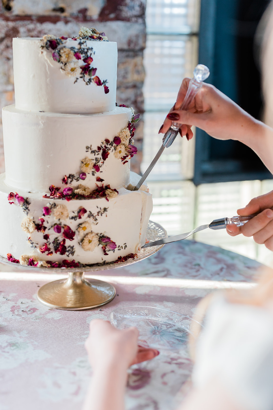 Three-tier floral cake being cut — dried flowers and brick wall behind — Tim Larsen Photography, Brainerd Lakes MN