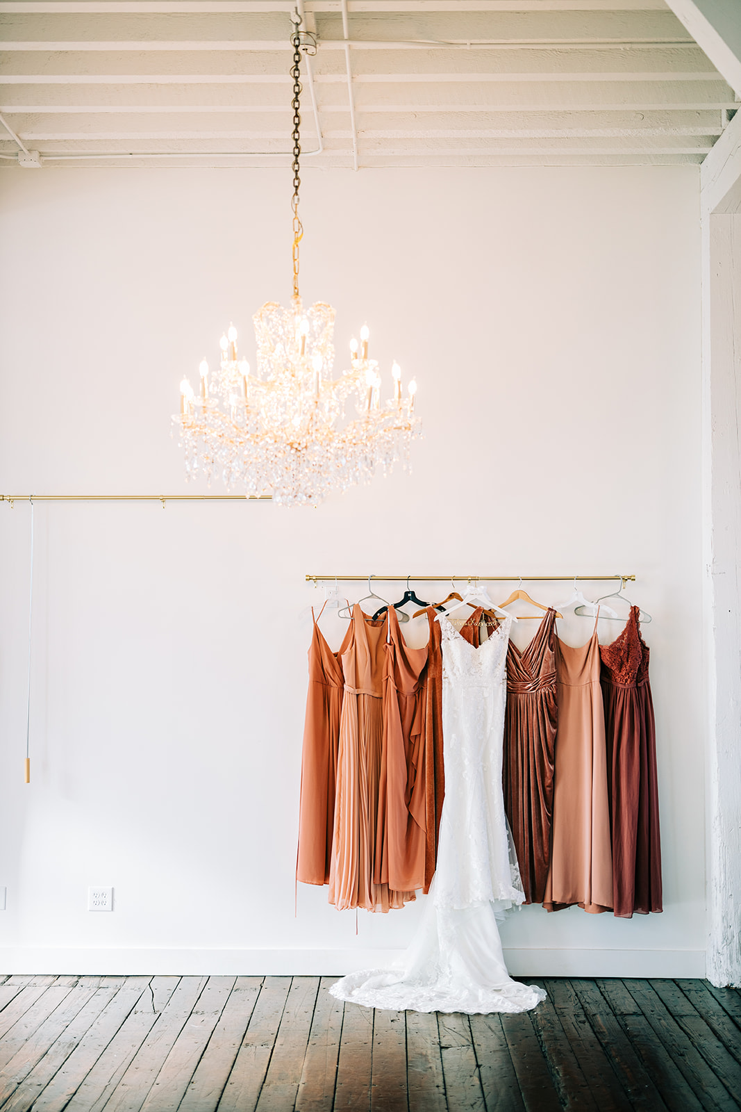 Bridesmaids dresses hanging on a rack with chandelier — rust and copper tones in the white room — Tim Larsen Photography, Brainerd Lakes MN