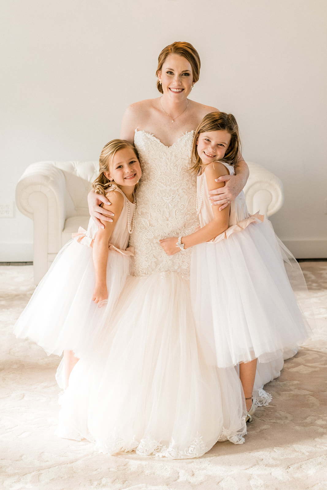 Bride with two flower girls in tulle dresses on the white couch in the bridal suite — Tim Larsen Photography, Brainerd Lakes MN