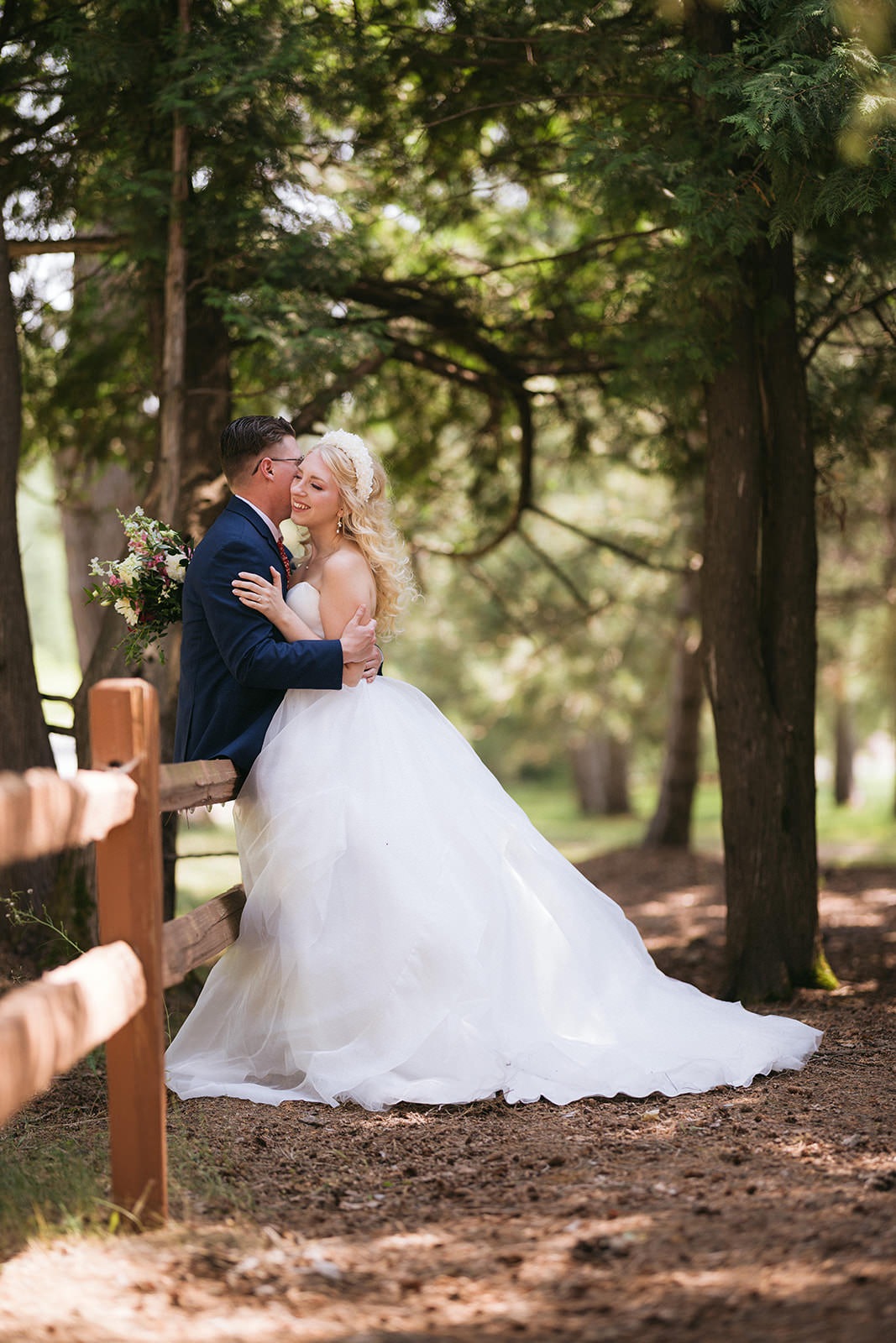 Couple kissing on a forest path by a wooden fence — soft pine tree light — Tim Larsen Photography, Brainerd Lakes MN