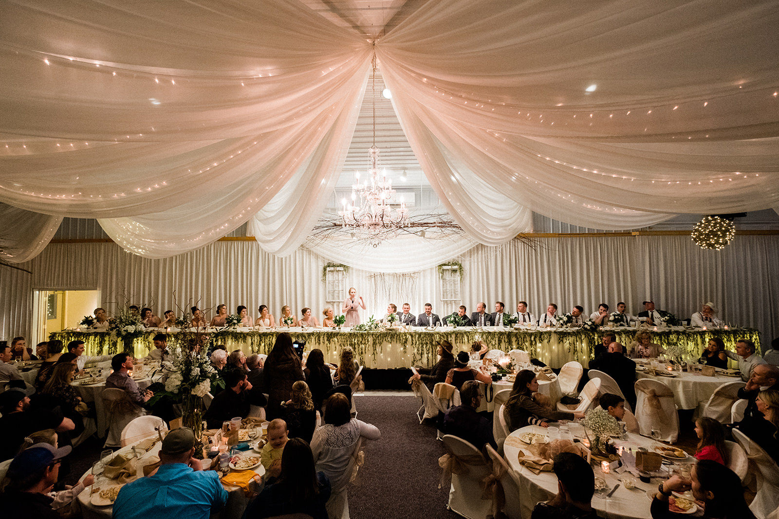 Wide reception room with draping, chandelier, and string lights — full house at Pine Peaks — Tim Larsen Photography, Brainerd Lakes MN