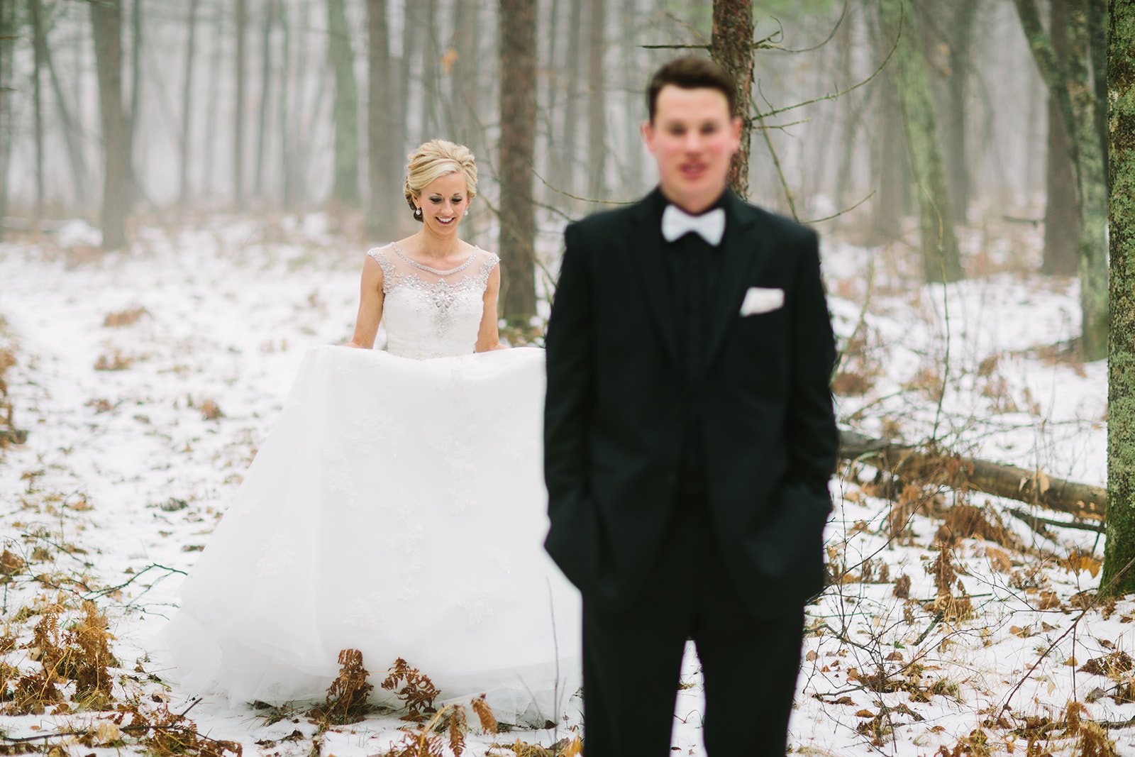 First look in snowy winter woods — bride approaching groom from behind — Tim Larsen Photography, Brainerd Lakes MN