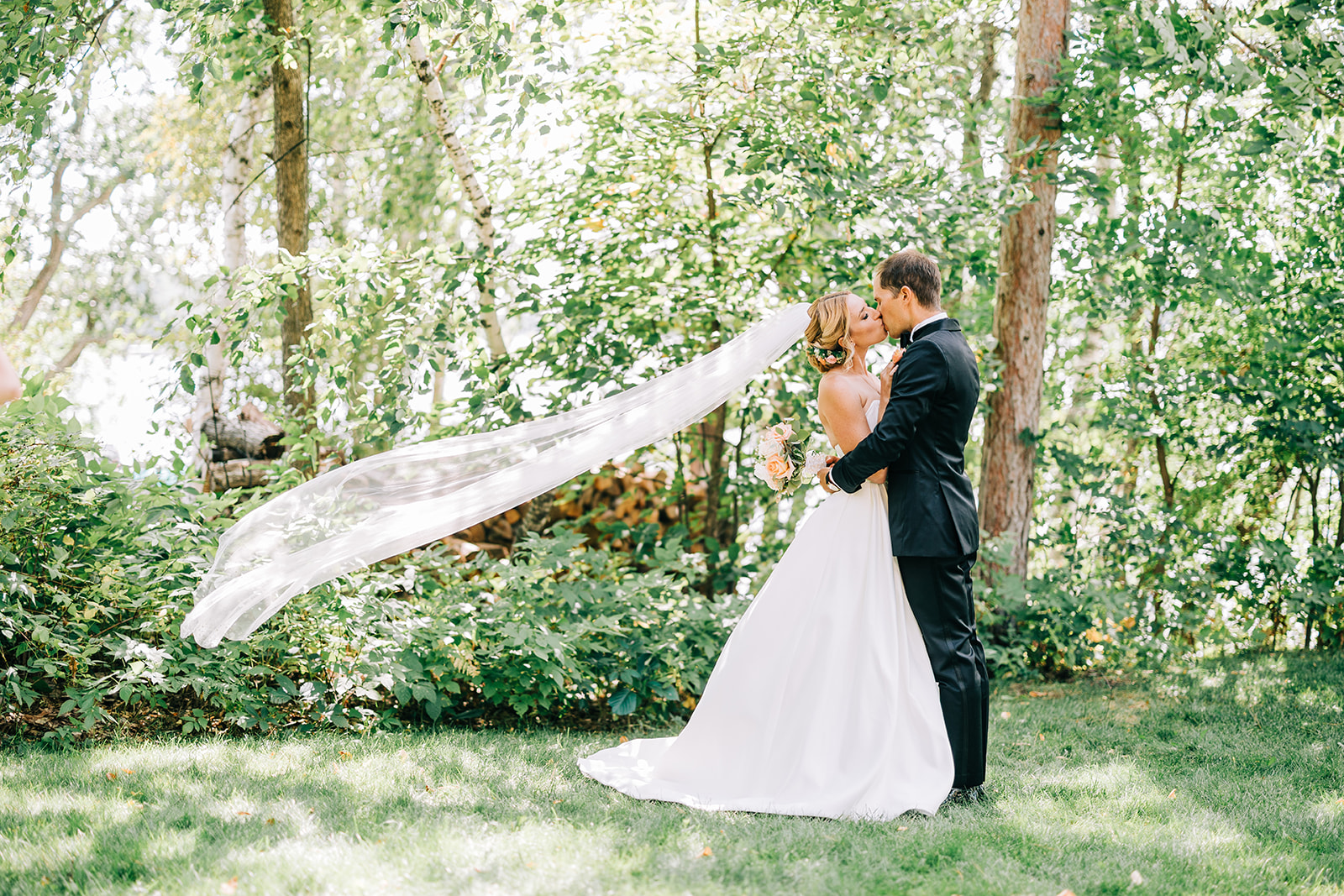 Couple embracing as veil catches the wind among sunlit trees — Tim Larsen Photography, Brainerd Lakes MN