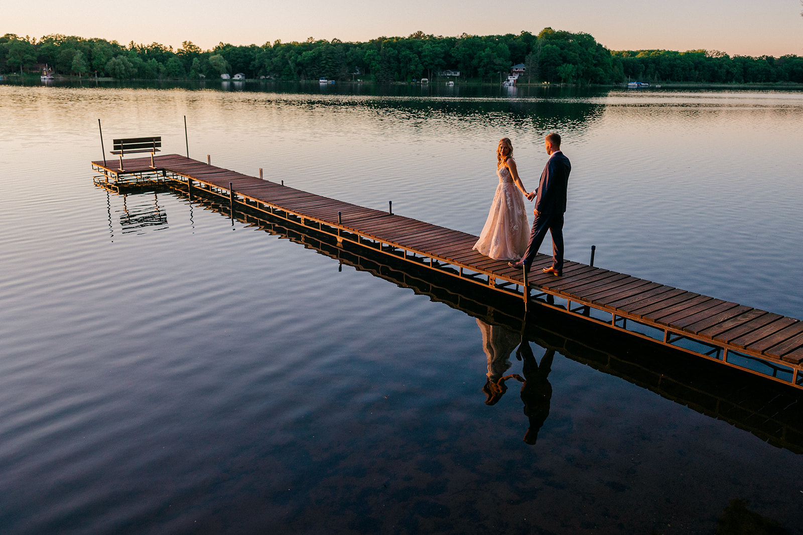 Couple walking hand in hand down a dock at sunset with lake reflection — Tim Larsen Photography, Brainerd Lakes MN