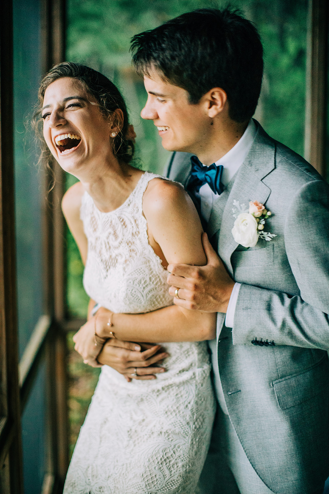 Groom embracing bride from behind as she laughs near cabin windows — Tim Larsen Photography, Brainerd Lakes MN