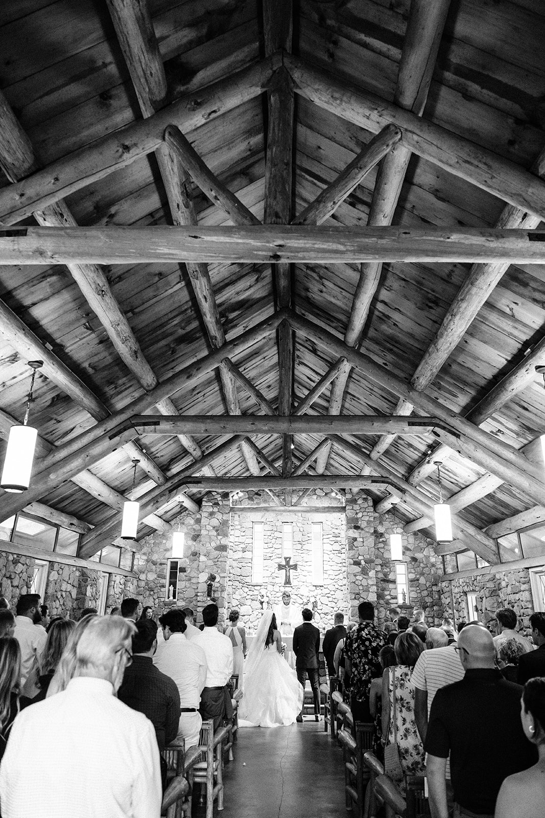 Ceremony inside a log-beam chapel with stone altar wall in black and white — Tim Larsen Photography, Brainerd Lakes MN