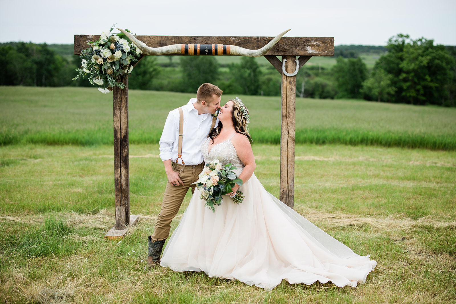 Couple kissing under a rustic wooden arch in an open country field — Tim Larsen Photography, Brainerd Lakes MN