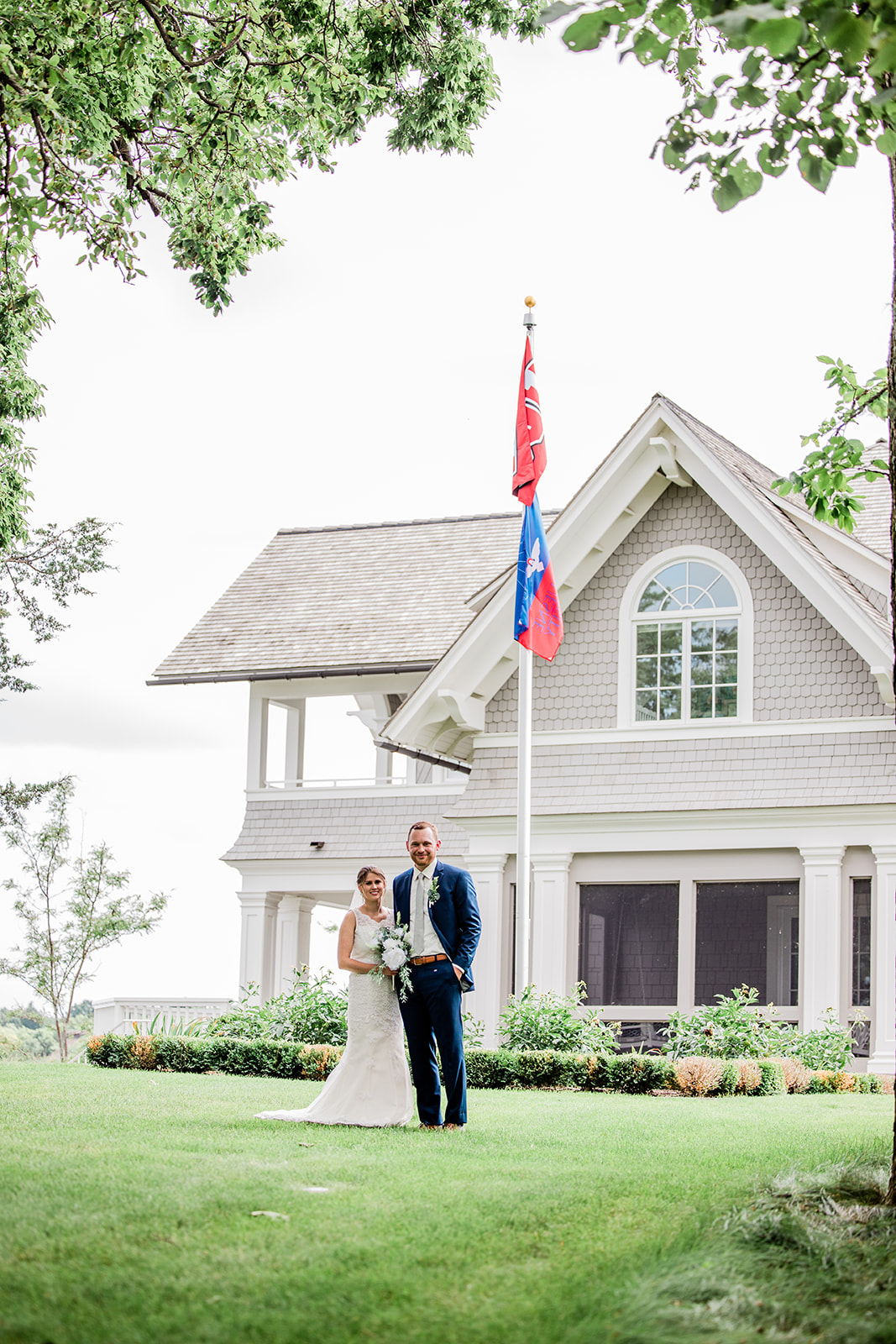 Couple standing on the lawn of a shingled lake cottage with flag — Tim Larsen Photography, Brainerd Lakes MN