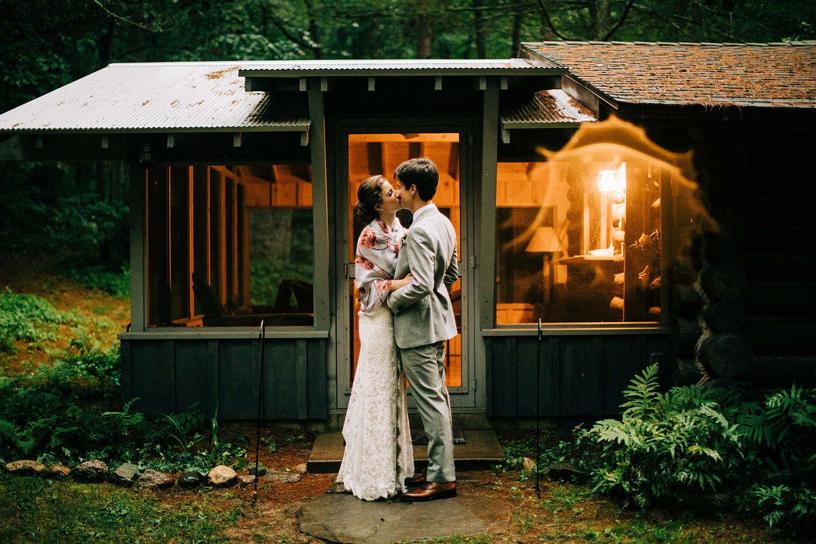 Couple embracing outside a warmly lit woodland cabin at twilight — Tim Larsen Photography, Brainerd Lakes MN