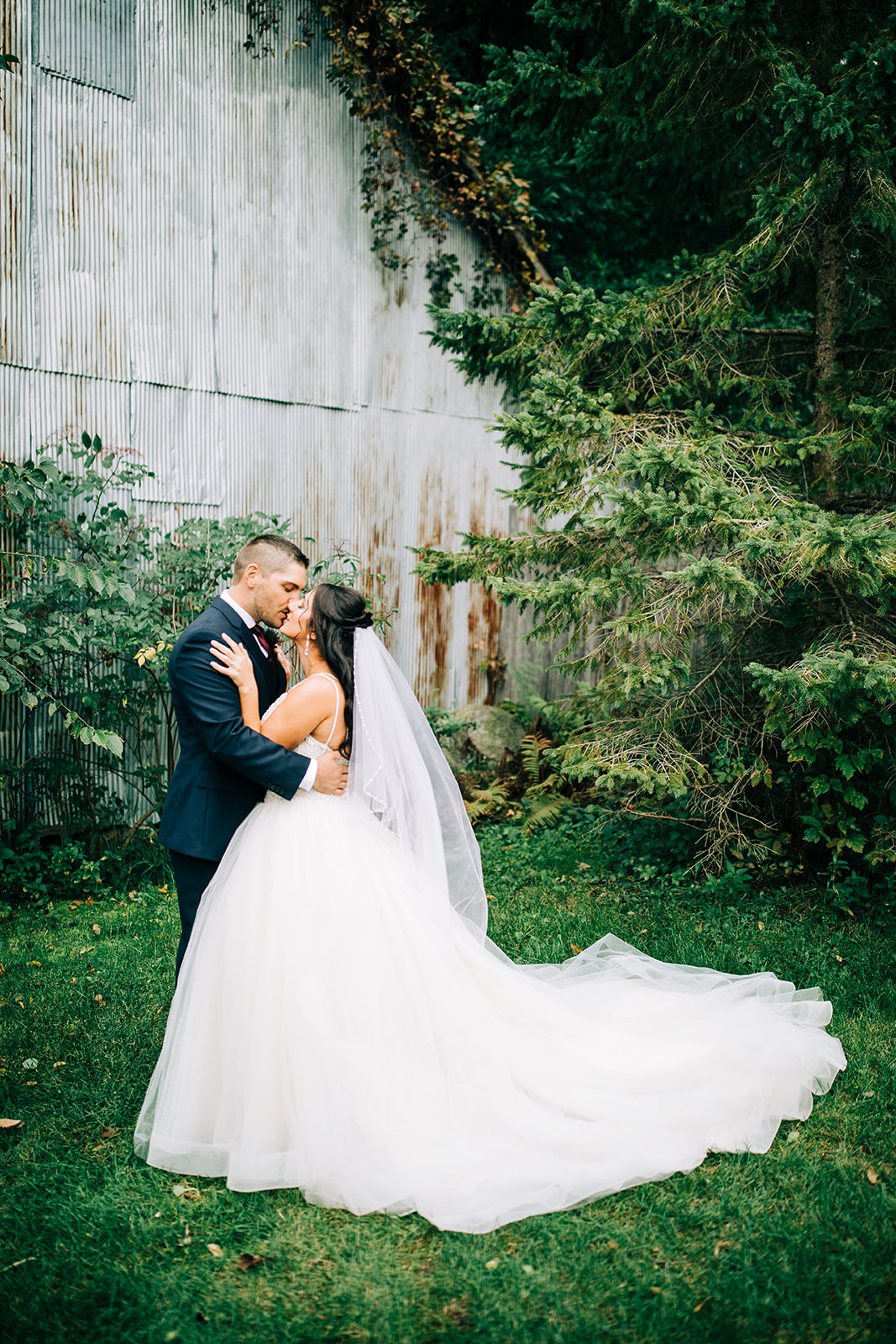 Couple embracing beside a weathered barn wall surrounded by evergreens — Tim Larsen Photography, Brainerd Lakes MN