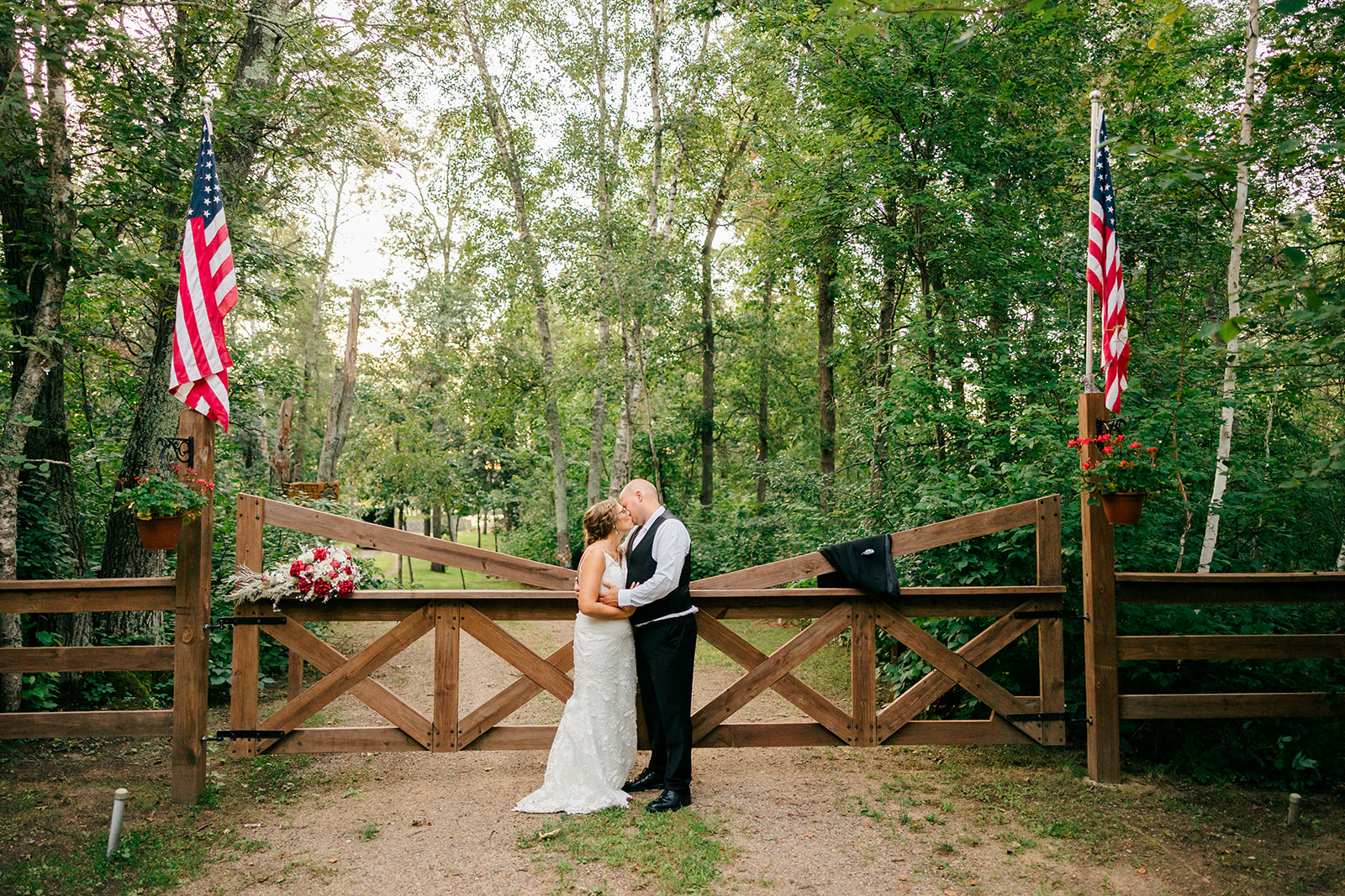 Couple kissing at a wooden gate with American flags in the summer woods — Tim Larsen Photography, Brainerd Lakes MN