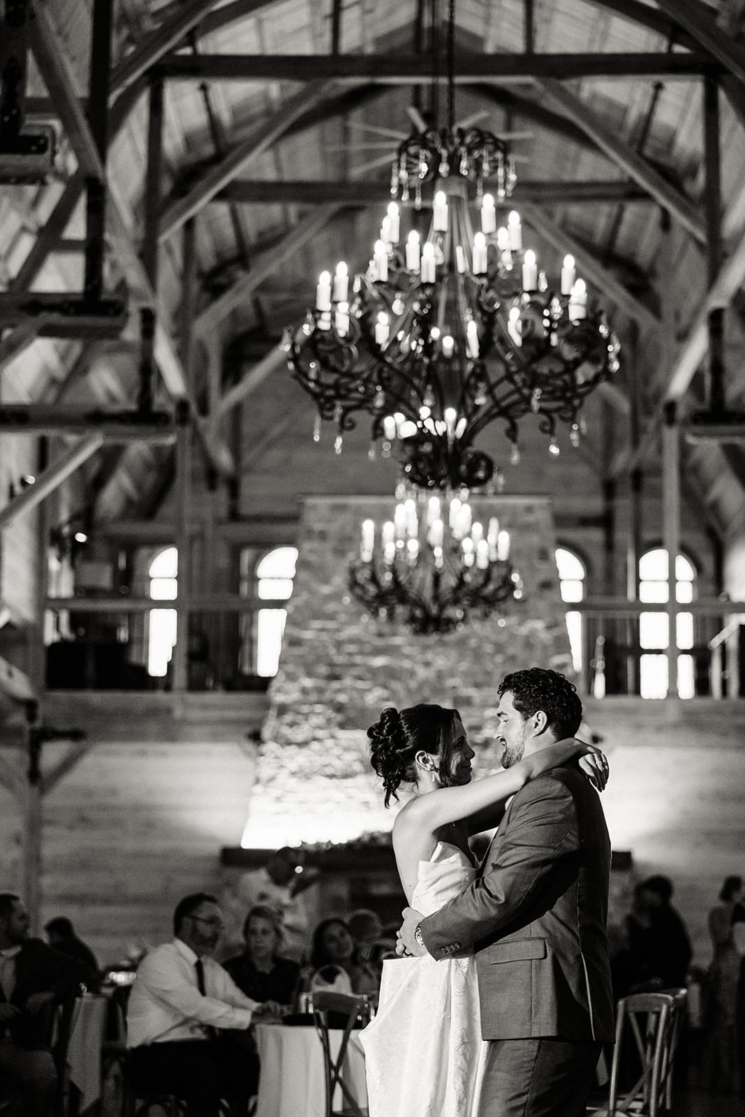 First dance in a barn venue with iron chandeliers and timber beams in black and white — Tim Larsen Photography, Brainerd Lakes MN