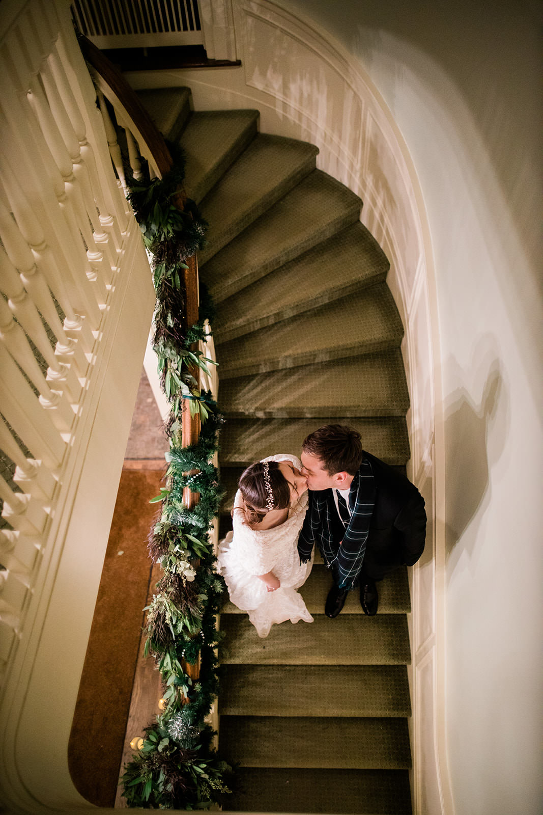 Couple kissing on a spiral staircase wrapped in greenery garland — winter wedding — Tim Larsen Photography, Brainerd Lakes MN