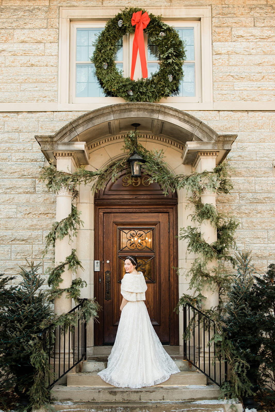 Bride in fur wrap on the steps of a stone estate decorated with holiday greenery and wreath — Tim Larsen Photography, Brainerd Lakes MN