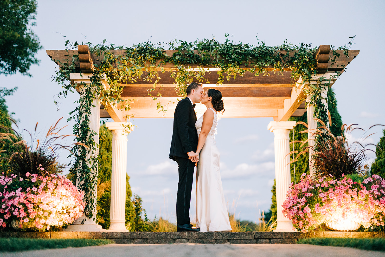Couple kissing under a lit pergola with flowers at twilight — garden estate reception — Tim Larsen Photography, Brainerd Lakes MN