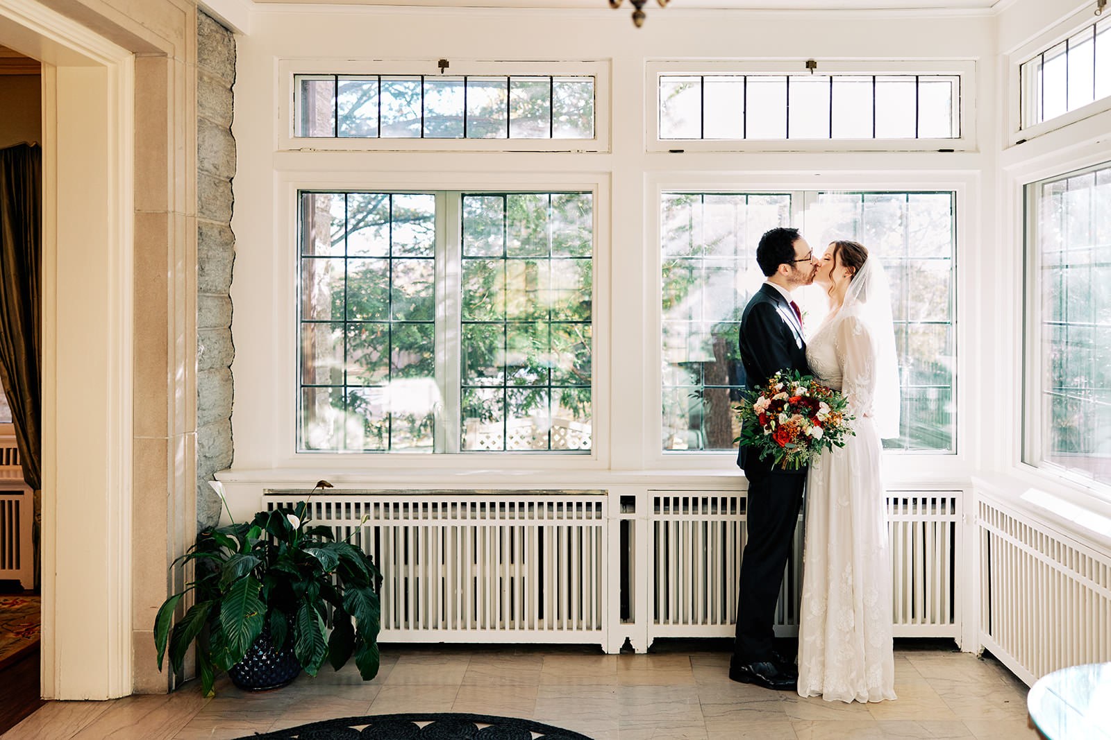 Couple kissing by the windows in a bright stone sunroom — Minneapolis estate wedding — Tim Larsen Photography, Brainerd Lakes MN