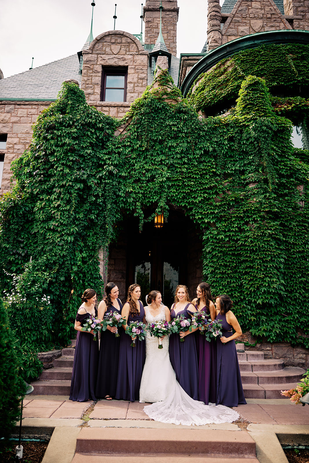 Bride with bridesmaids in purple dresses in front of an ivy-covered stone mansion — Tim Larsen Photography, Brainerd Lakes MN