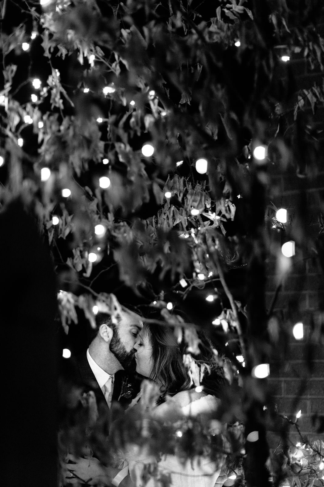 Couple kissing through string lights at night at Whitefish Lodge — Tim Larsen Photography, Brainerd Lakes MN