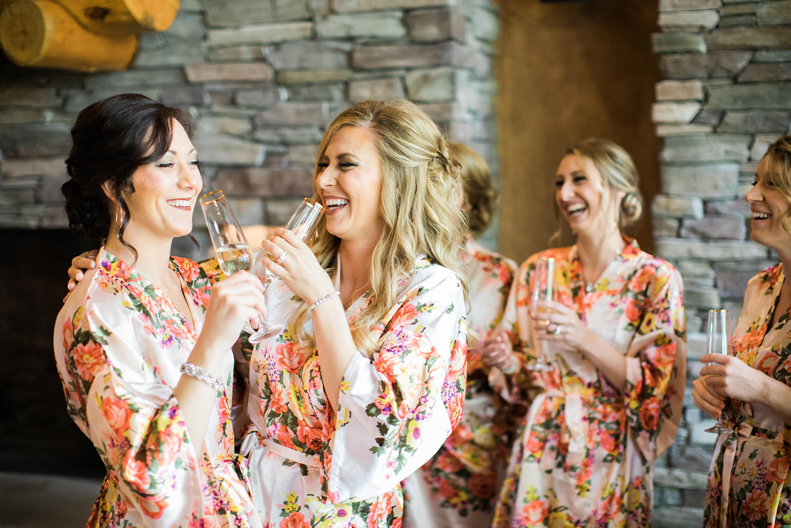 Bridesmaids in floral robes toasting champagne by the stone fireplace — Tim Larsen Photography, Brainerd Lakes MN