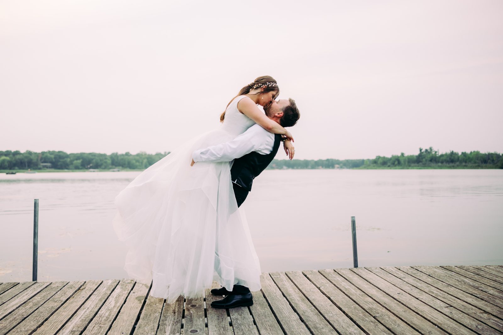 Centered couple on weathered dock, lake and treeline stretching wide behind them. — Tim Larsen Photography, Brainerd Lakes MN
