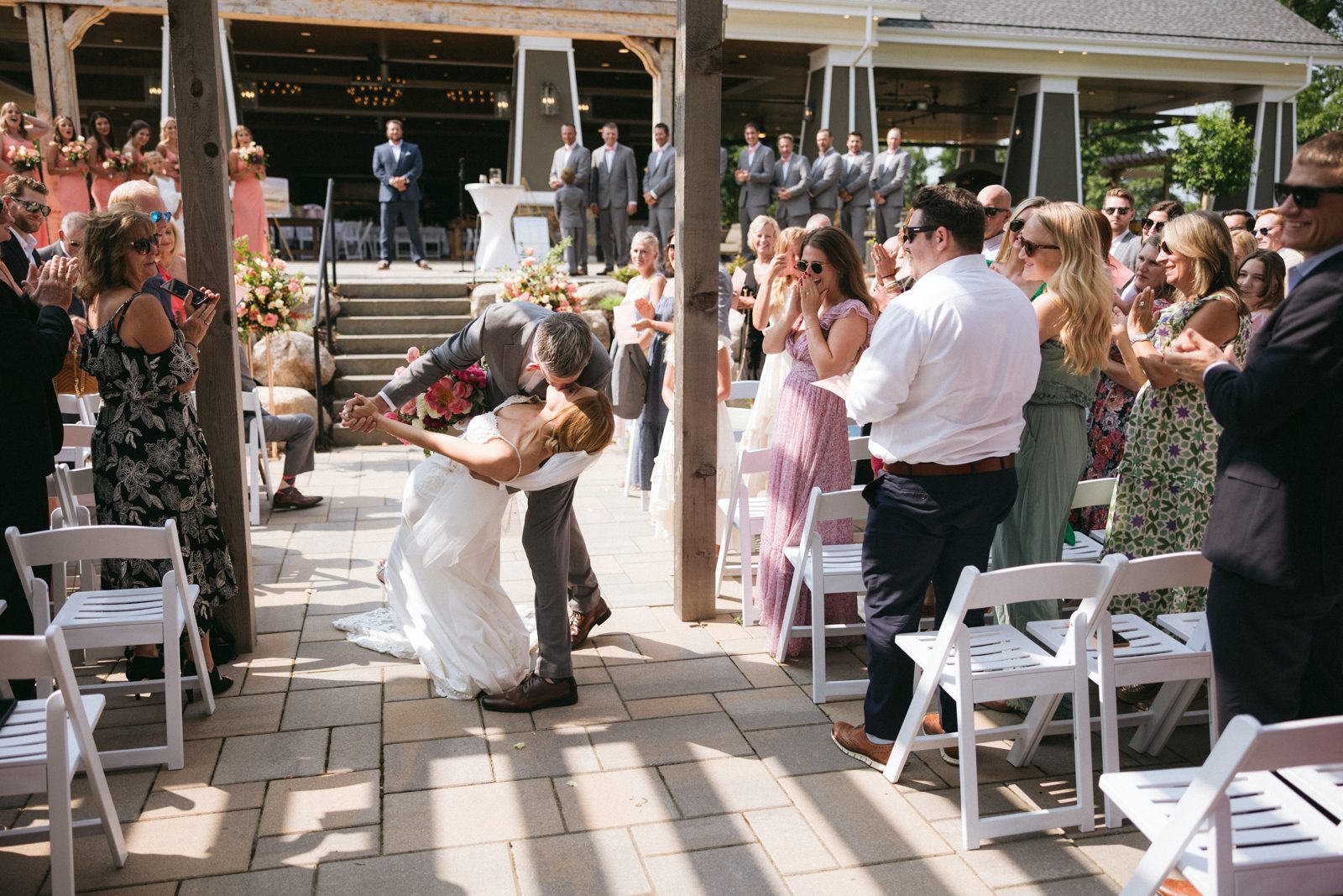 Couple dips mid-aisle as guests cheer from both sides, leading lines to pavilion. — Tim Larsen Photography, Brainerd Lakes MN