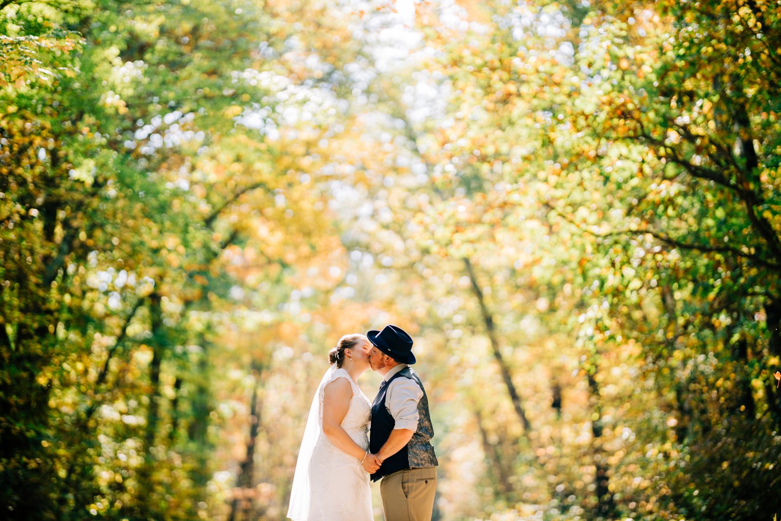 Couple small in lower frame, towering backlit autumn canopy fills space above. — Tim Larsen Photography, Brainerd Lakes MN