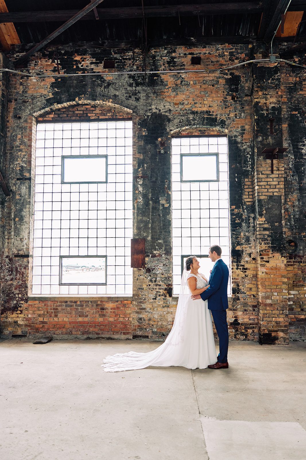 Couple dwarfed by towering arched factory windows and weathered brick walls. — Tim Larsen Photography, Brainerd Lakes MN
