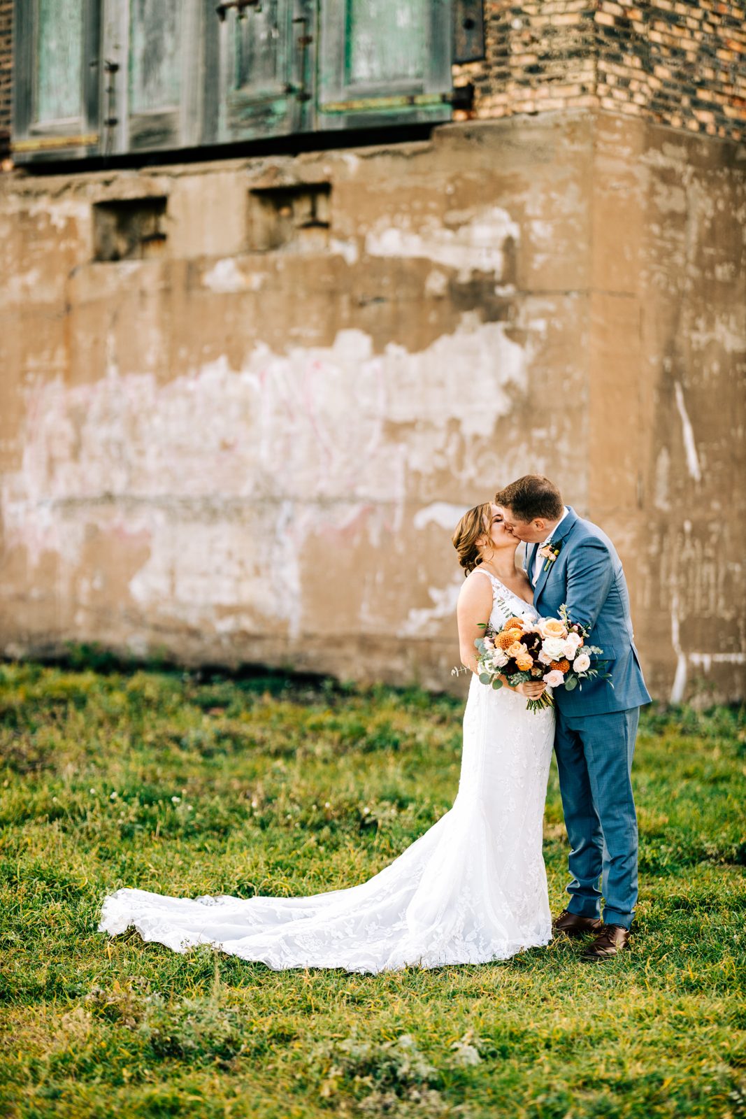 Couple anchored bottom-right against weathered wall; green shuttered window crowns the frame. — Tim Larsen Photography, Brainerd Lakes MN