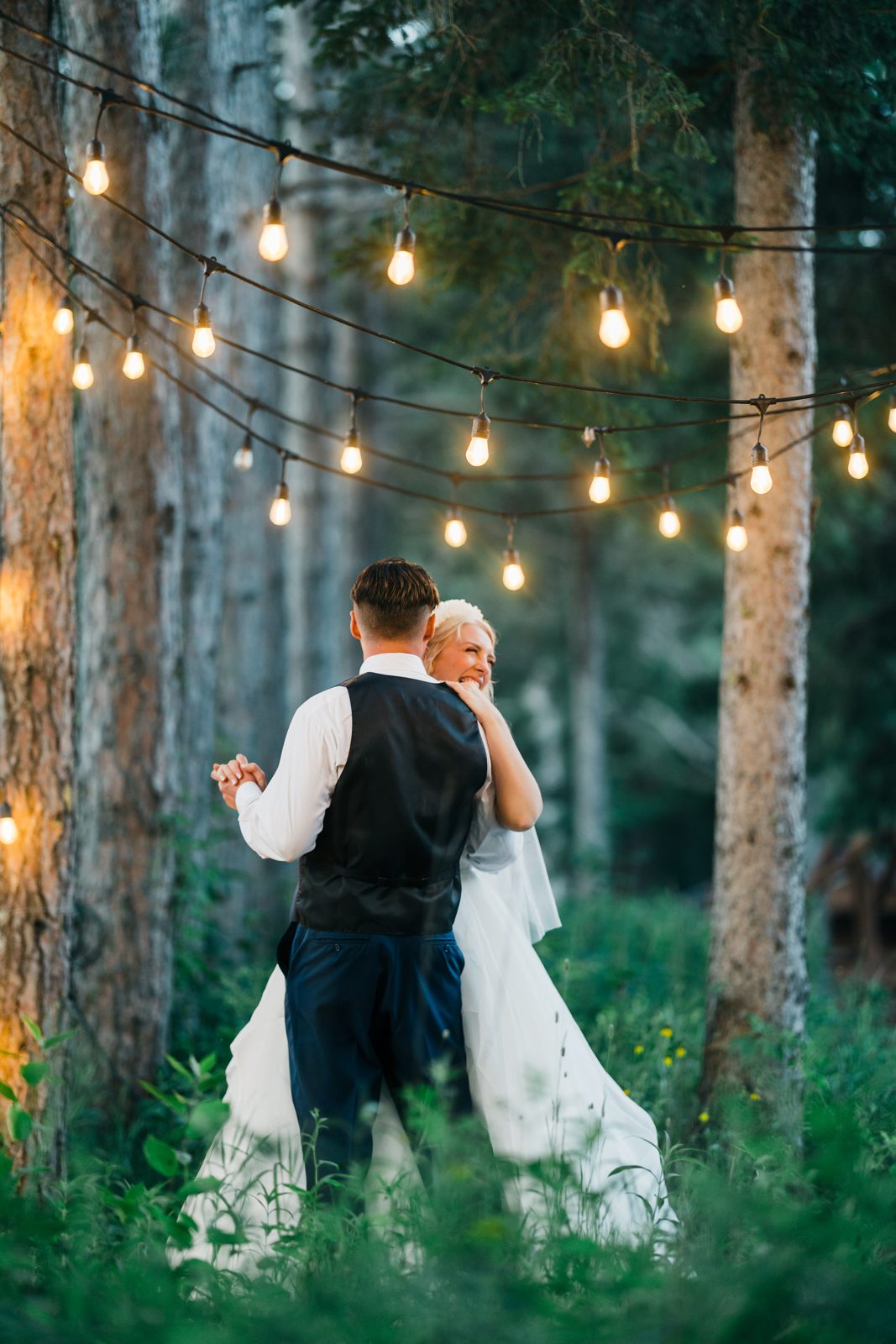 Tall pines frame couple beneath layered cafe lights at dusk — Tim Larsen Photography, Brainerd Lakes MN