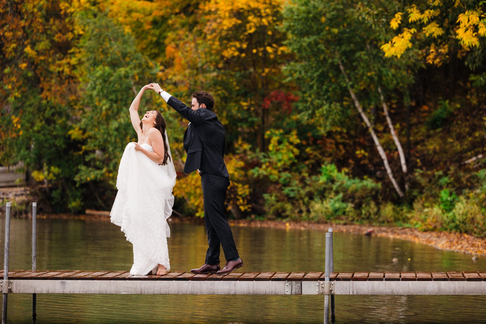 Couple twirling on dock framed by autumn foliage and lake reflection. — Tim Larsen Photography, Brainerd Lakes MN