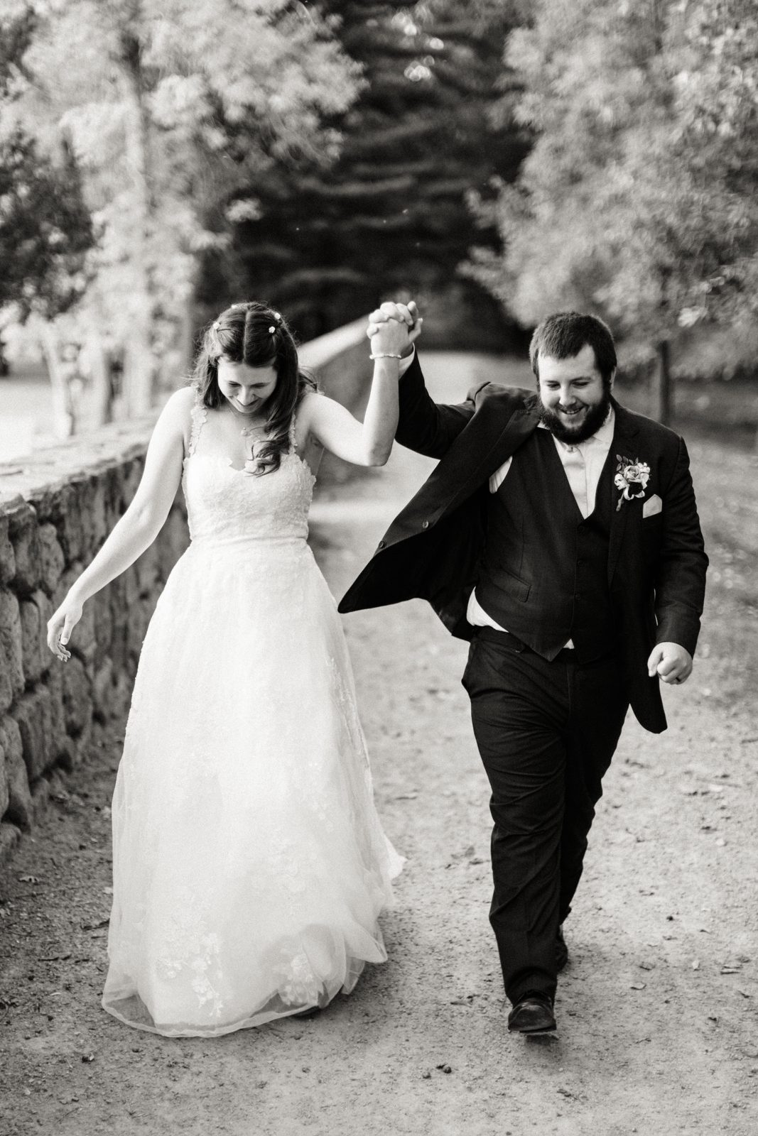 Couple mid-stride, joined hands raised overhead, both grinning downward in shared laughter. — Tim Larsen Photography, Brainerd Lakes MN