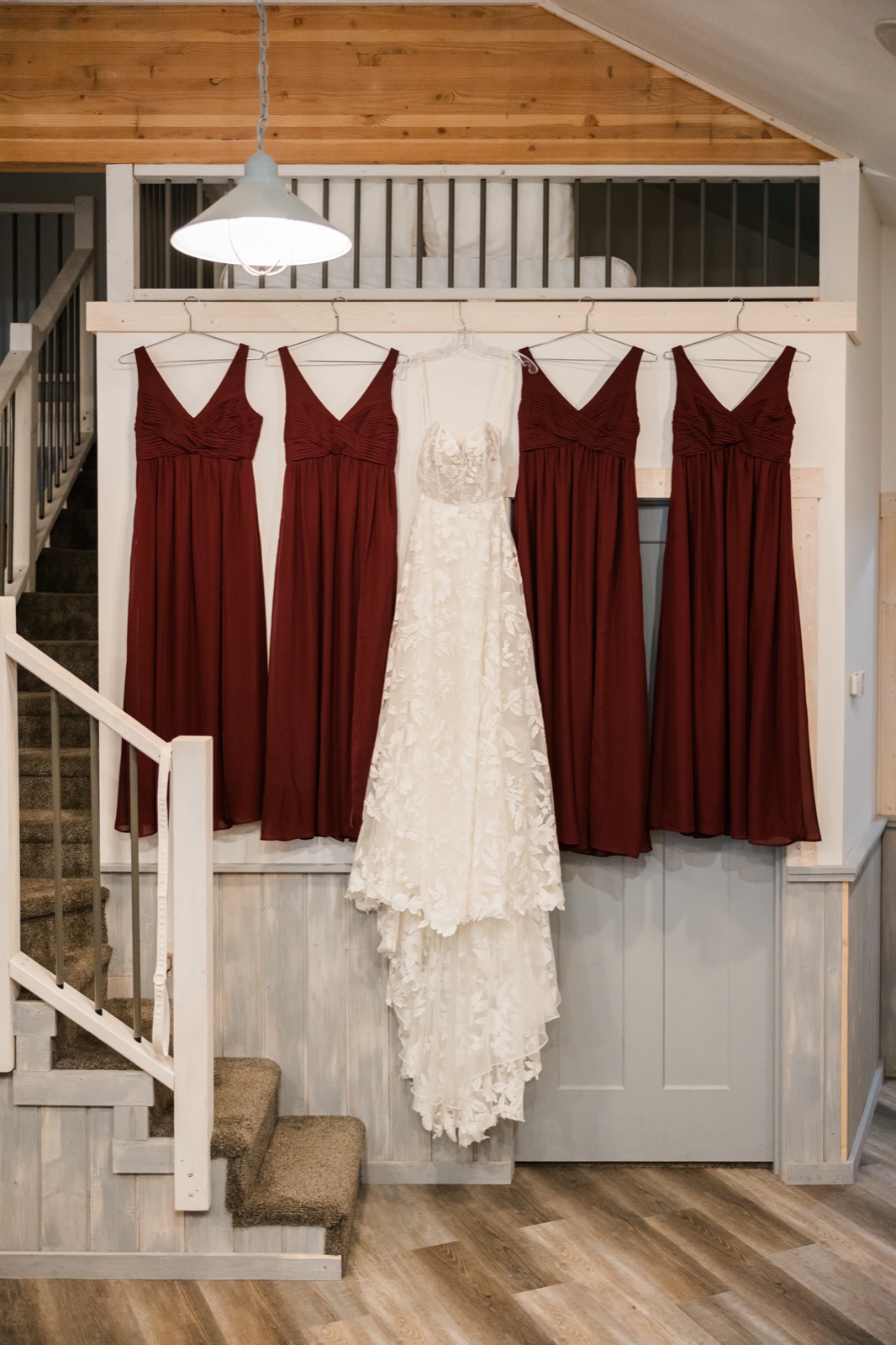 Bridal gown hung centered between four burgundy bridesmaid dresses on a wooden railing at Manhattan Beach Lodge — Tim Larsen Photography, Brainerd Lakes MN