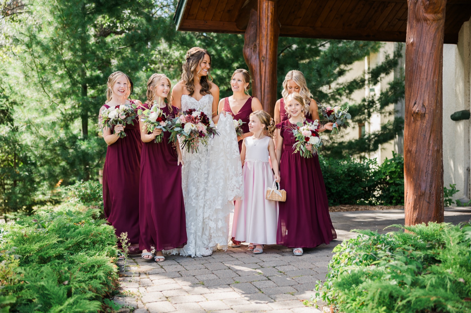 Bride walks with bridesmaids beneath the timber entrance pavilion at Manhattan Beach Lodge — Tim Larsen Photography, Brainerd Lakes MN