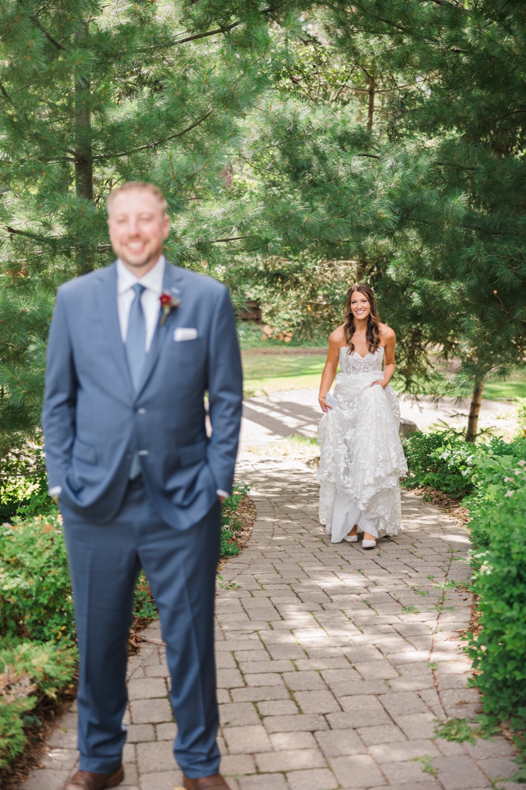 Bride walks down a brick garden path toward the groom before their first look at Manhattan Beach Lodge — Tim Larsen Photography, Brainerd Lakes MN
