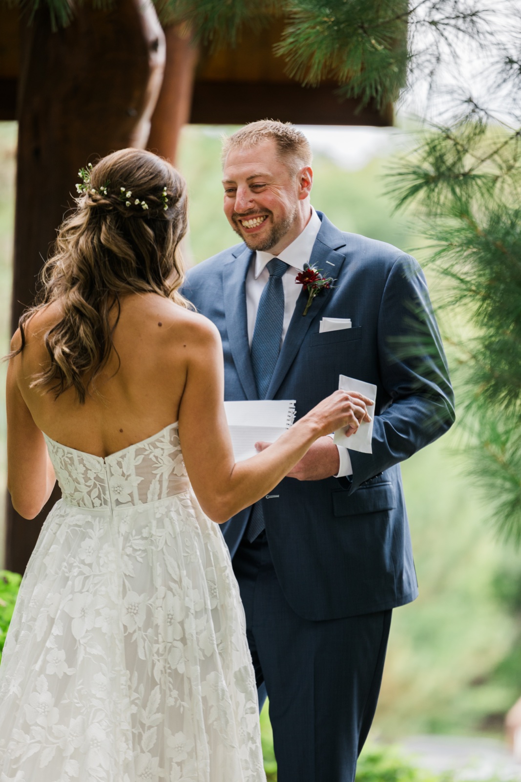 Groom beams at the bride as she reads her vows beneath the wooden ceremony arbor at Manhattan Beach Lodge — Tim Larsen Photography, Brainerd Lakes MN