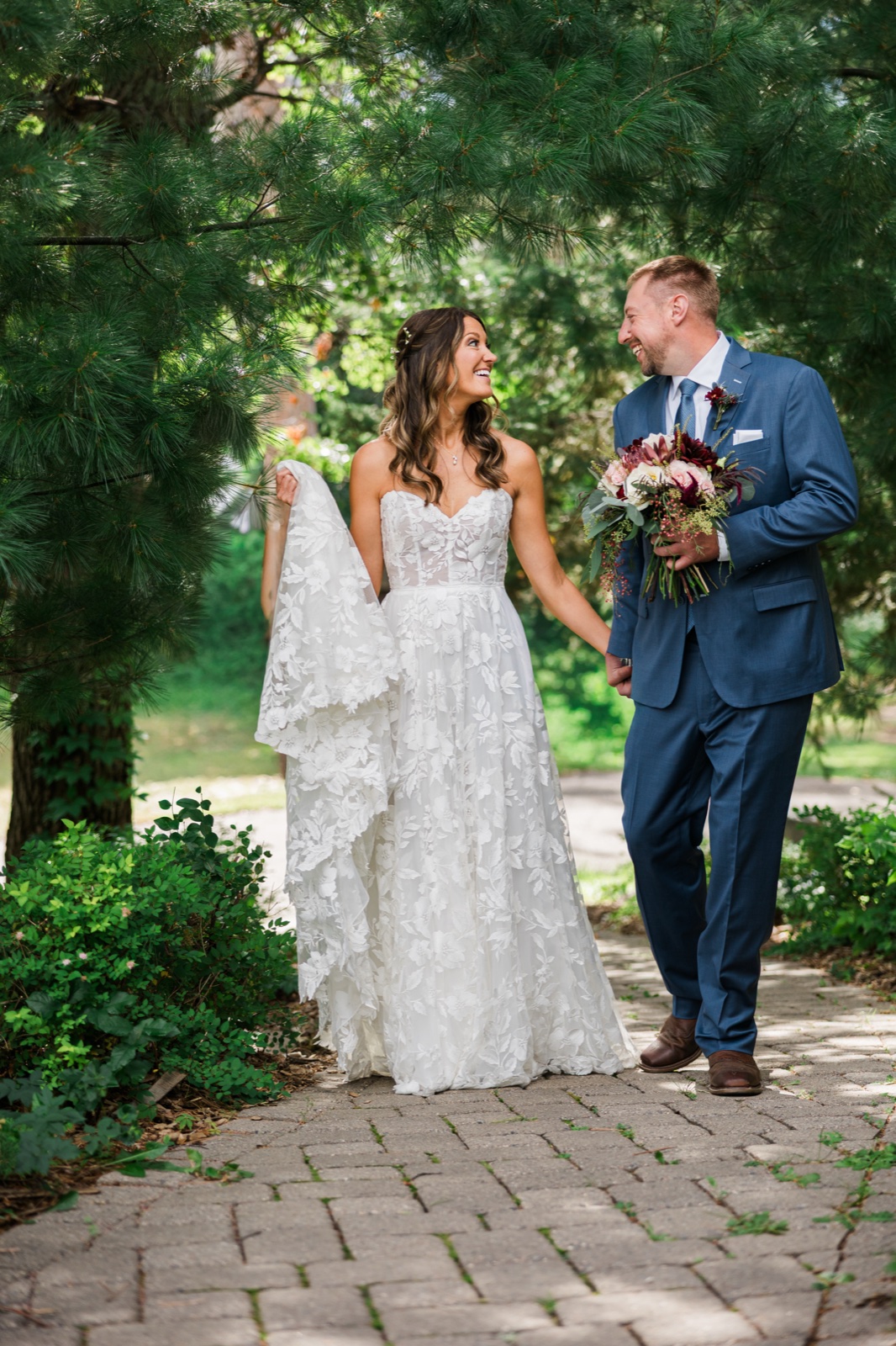 Bride and groom walk hand-in-hand beneath pine boughs on the garden path at Manhattan Beach Lodge — Tim Larsen Photography, Brainerd Lakes MN