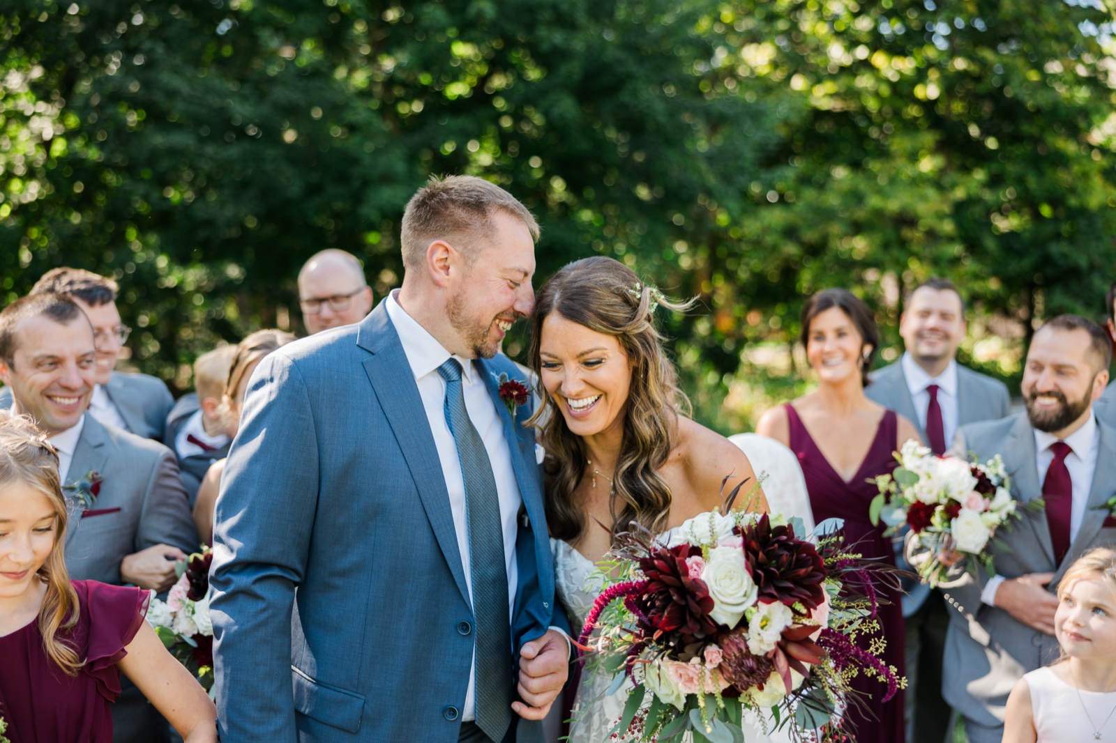 Bride laughs with the groom surrounded by the bridal party on a tree-lined lawn at Manhattan Beach Lodge — Tim Larsen Photography, Brainerd Lakes MN