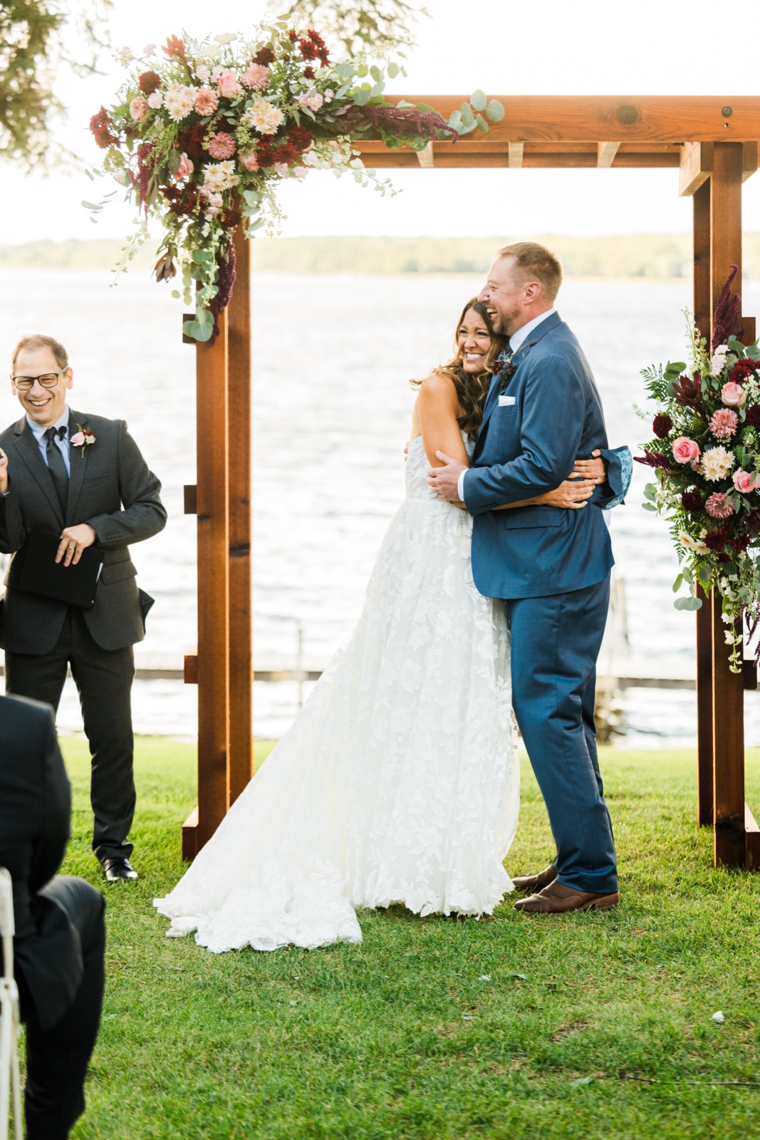 Bride and groom embrace after vows under the floral arch at the lakeside ceremony on Big Trout Lake — Tim Larsen Photography, Brainerd Lakes MN