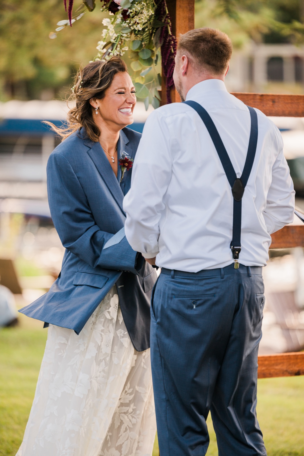 Bride laughs joyfully with the groom under the floral arch at the lakeside ceremony on Big Trout Lake — Tim Larsen Photography, Brainerd Lakes MN