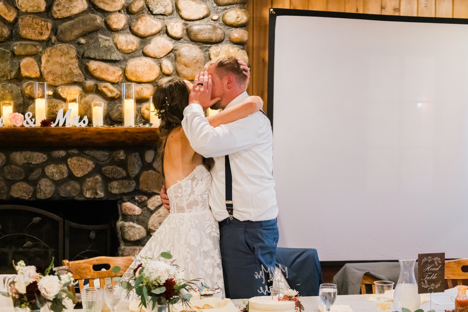 Bride holds the grooms face as they kiss at the head table by the stone fireplace at Manhattan Beach Lodge — Tim Larsen Photography, Brainerd Lakes MN