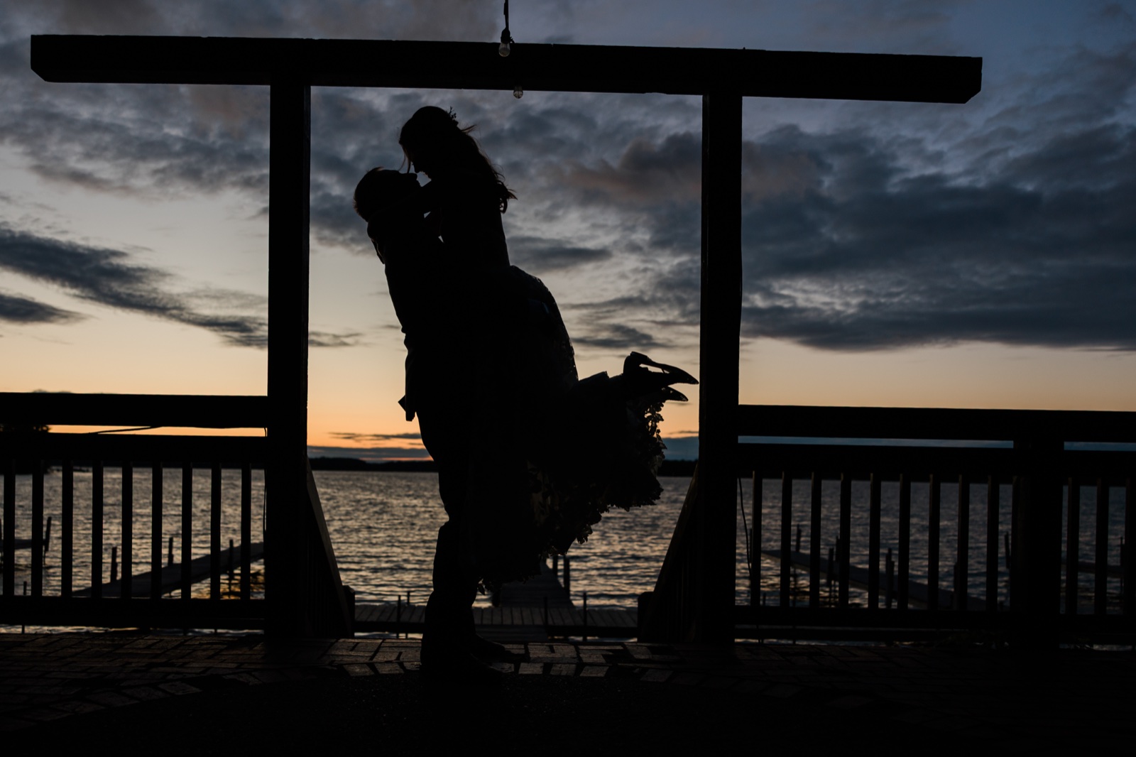 Groom lifts the bride into a kiss under the pergola at the end of the Manhattan Beach Lodge dock at dusk — Tim Larsen Photography, Brainerd Lakes MN