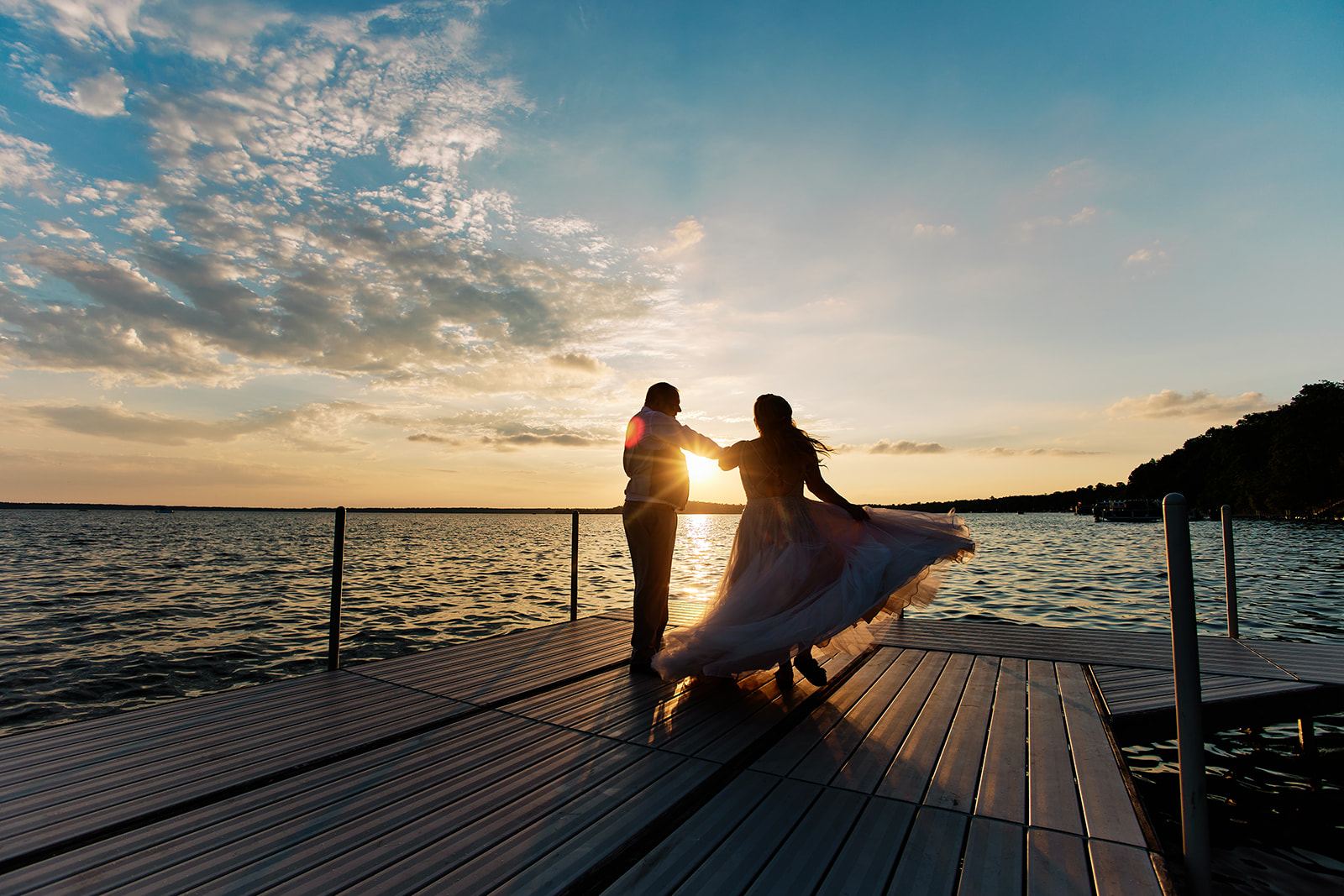 A bride and groom twirl in silhouette at the end of a long dock as the sun flares between them over Gull Lake at sunset — Tim Larsen Photography, Brainerd Lakes MN