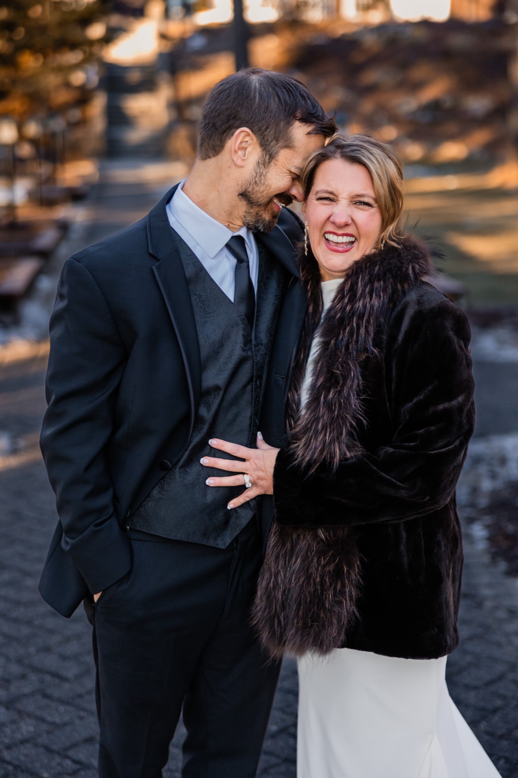 The bride laughs openly in a dark fur coat while the groom leans his forehead against hers, both backlit by low winter sun at Grand View Lodge — Tim Larsen Photography, Brainerd Lakes MN