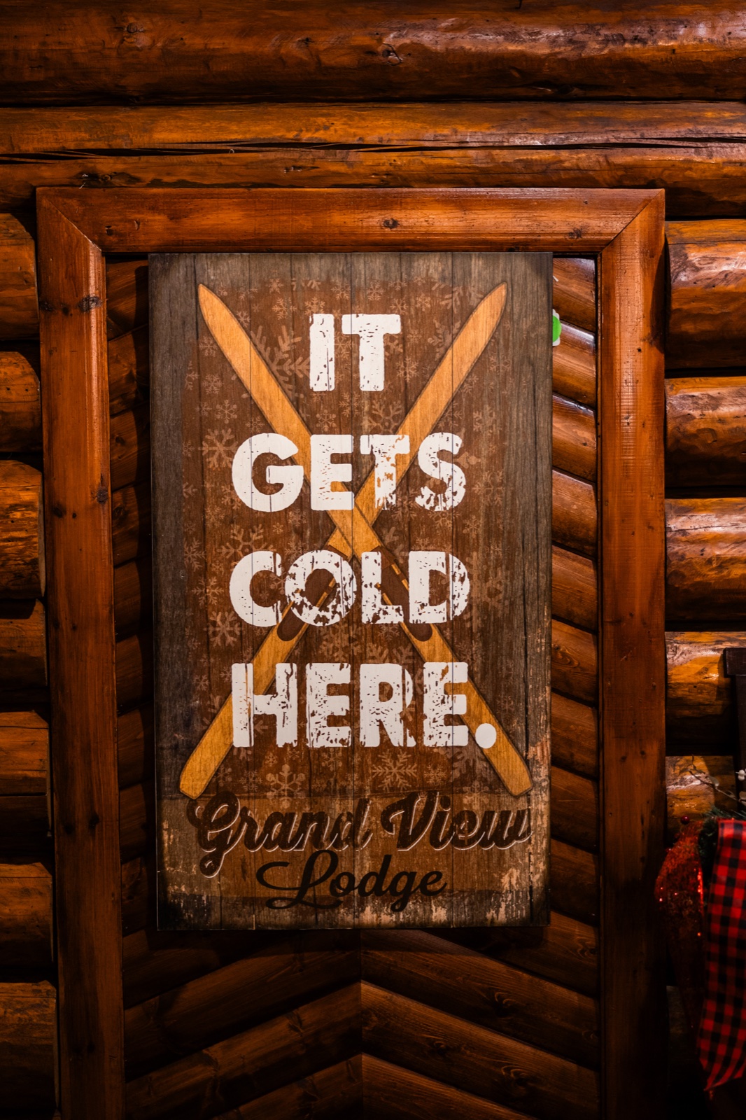 A rustic wooden sign reading "It Gets Cold Here — Grand View Lodge" with crossed skis, mounted on a log cabin wall — Tim Larsen Photography, Brainerd Lakes MN